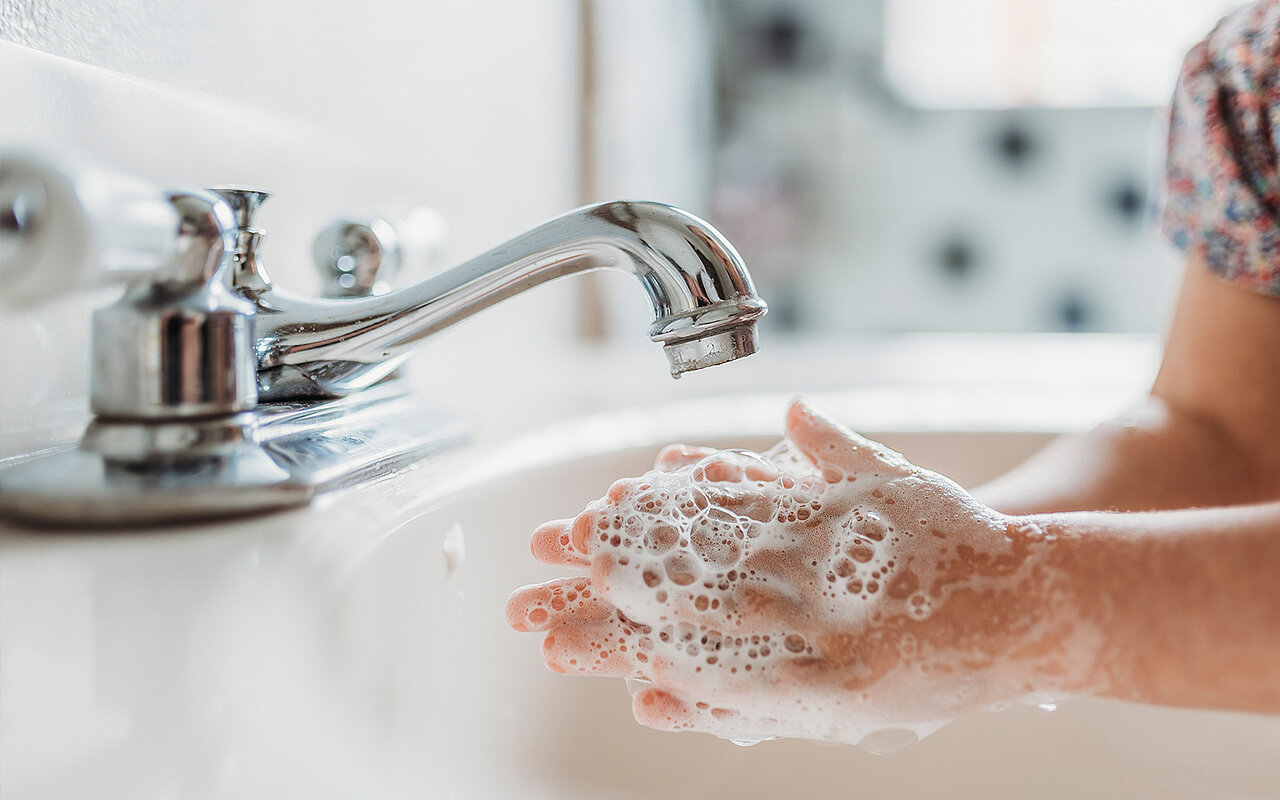 Hände waschen mit Seife unter einem laufenden Wasserhahn