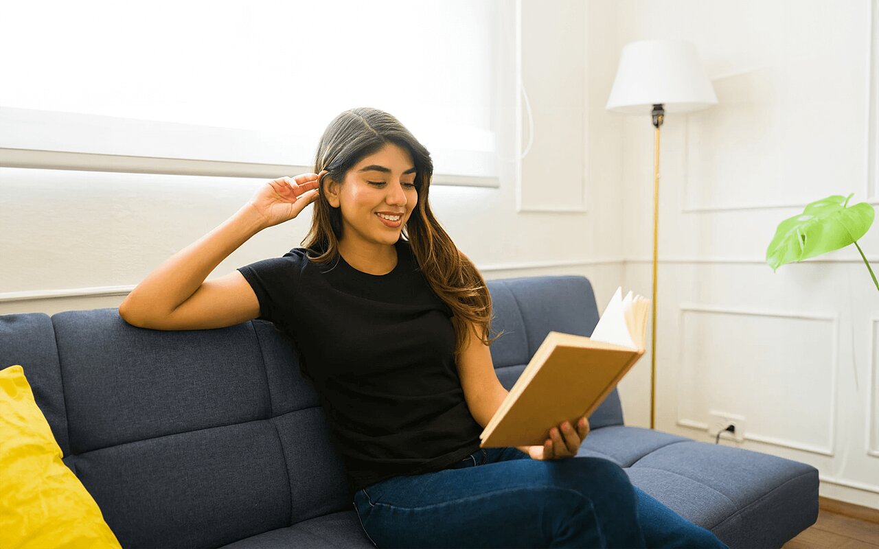 Eine Frau mit einem schwarzen Top sitzt auf der Couch und liest ein Buch