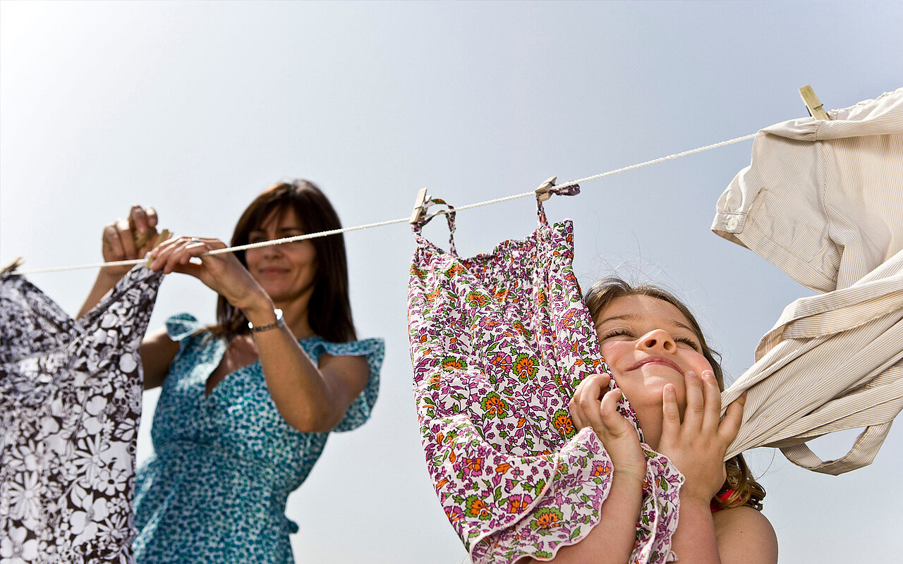 Eine Frau hängt die Wäsche an einer Wäscheleine im Garten aus